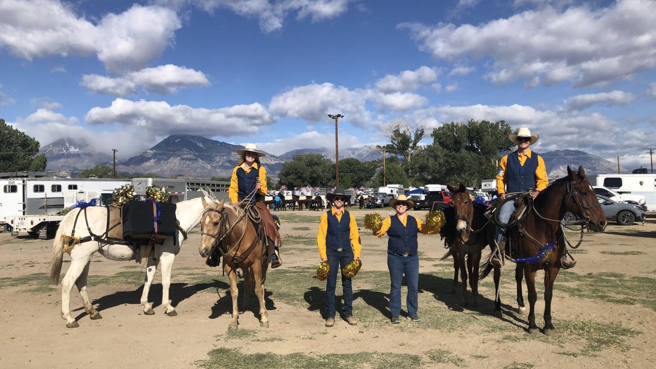 Students dressed in blue and gold western wear. Two students are atop horses and two students are cheering them on by holding pom poms.